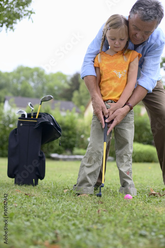 Senior adult man is teaching a girl how to play golf, selective focus