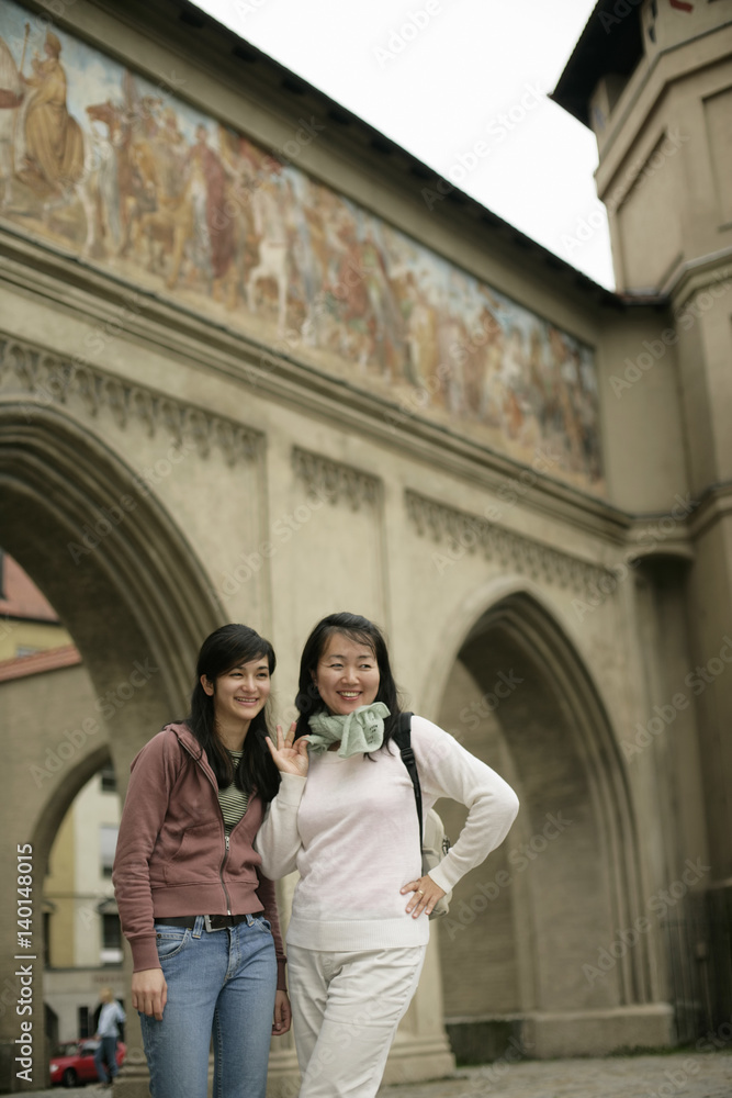 Two young Asian women standing in front of a painted gate, selective focus