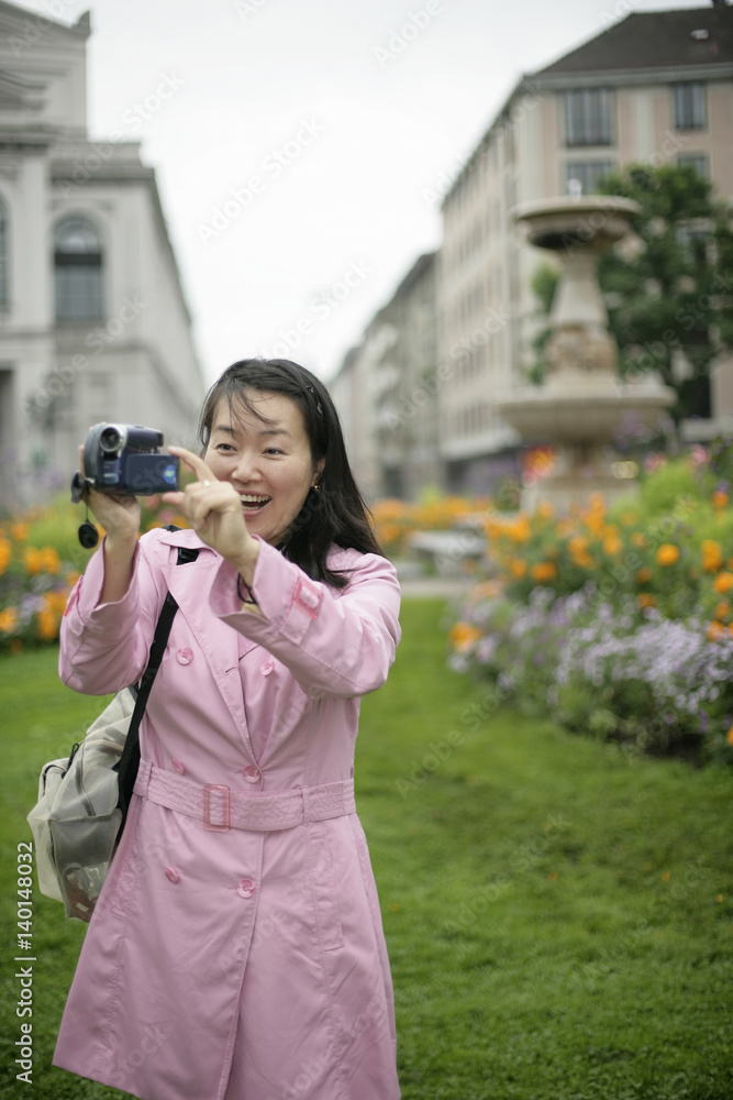 Young Asian woman with a camera standing in front of a park and is laughing, selective focus