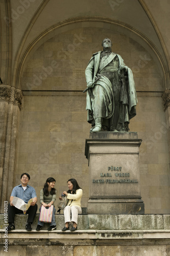 Three Asian people sitting on the top stairs of a monument