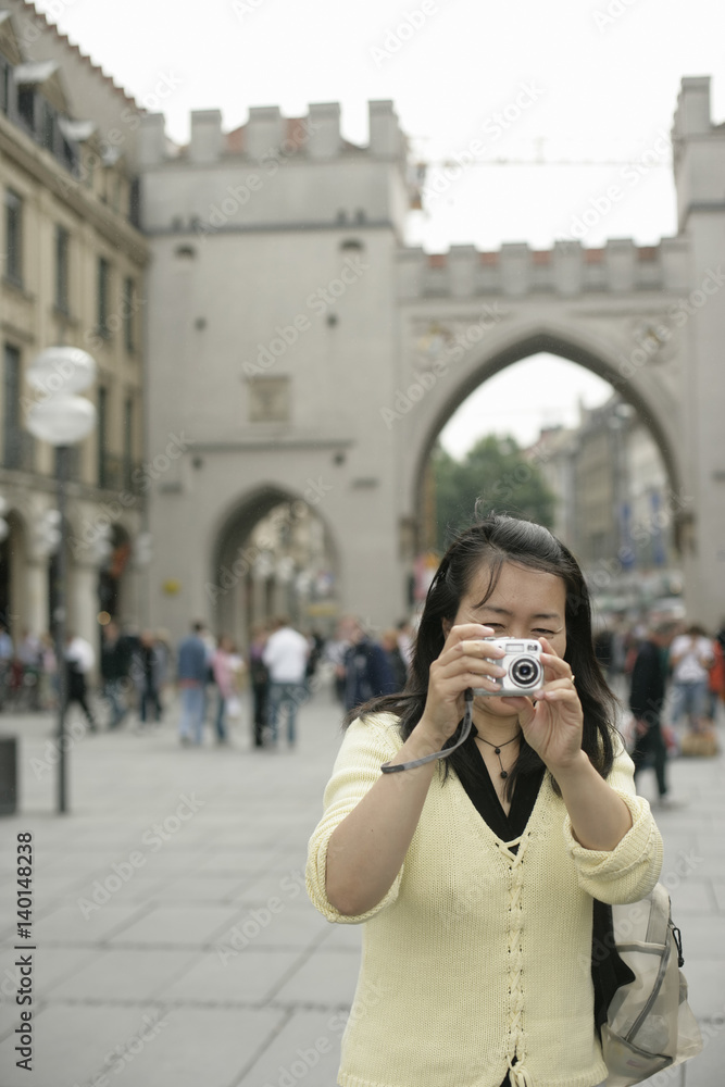 Young Asian woman with a camera standing in front of a big ancient gate, selective focus