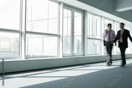 Two businessmen walking through a company hall talking about business