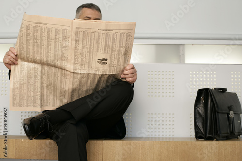Businessman sitting on a bench reading a newspaper
