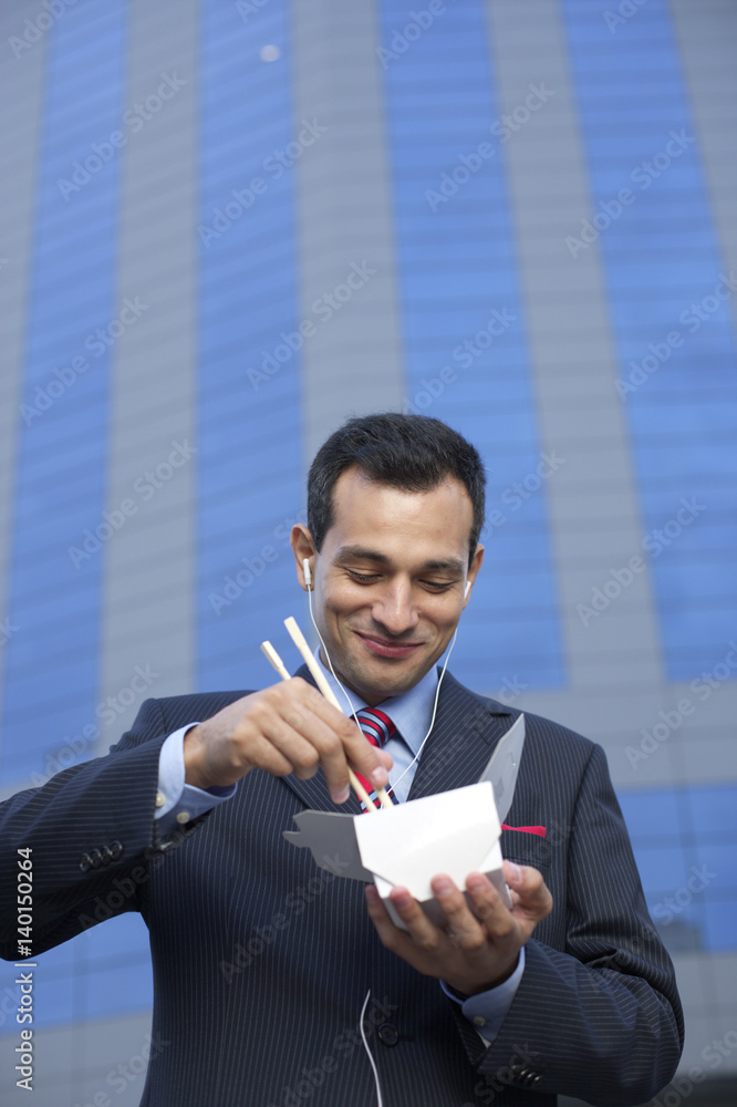 Businessman with earphones eating Asian food Businessman with earphones eating Asian food