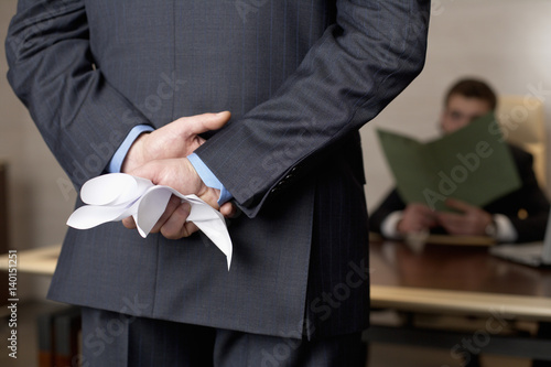 Businessman crushing a document behind his back