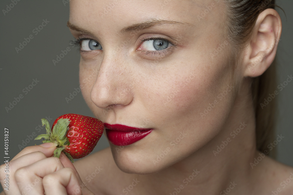 Young woman with a red strawberry under her red lips (part of), close-up Young woman with a red strawberry under her red lips (part of), close-up