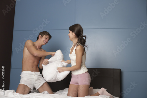 Young brunette woman punshing her boyfriend laughing with pillows photo