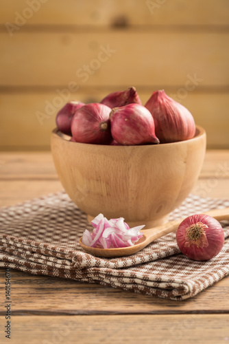 Sliced onion in spoon and red onion in bowl on wood table.