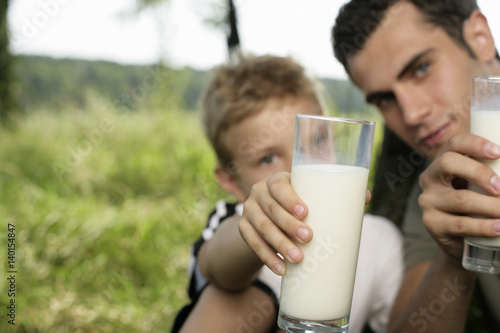 Father and son holding glasses of milk at camera
