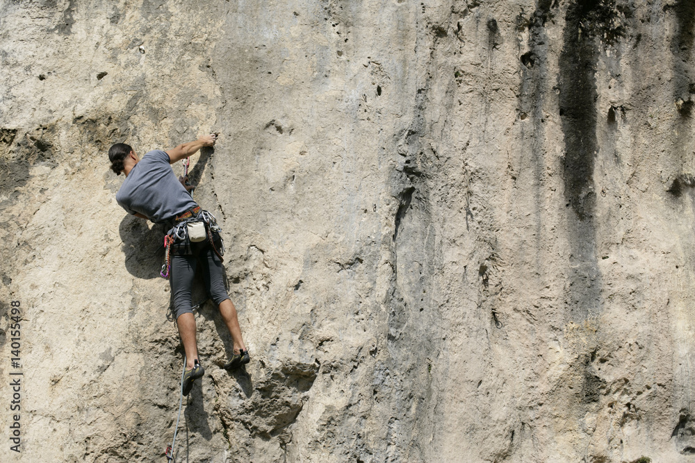 Young man with black hair climbing up a rocky wall, selective focus