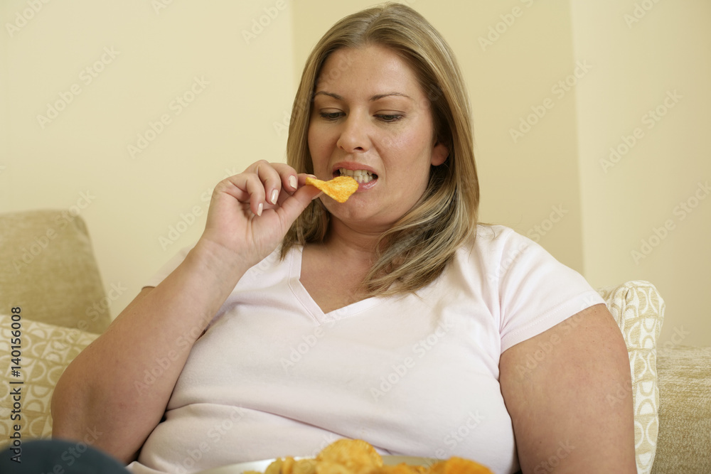 Overweight woman on a settee is eating crips from a bowl (part of), close-up Overweight woman on a settee is eating crips from a bowl (part of), close-up