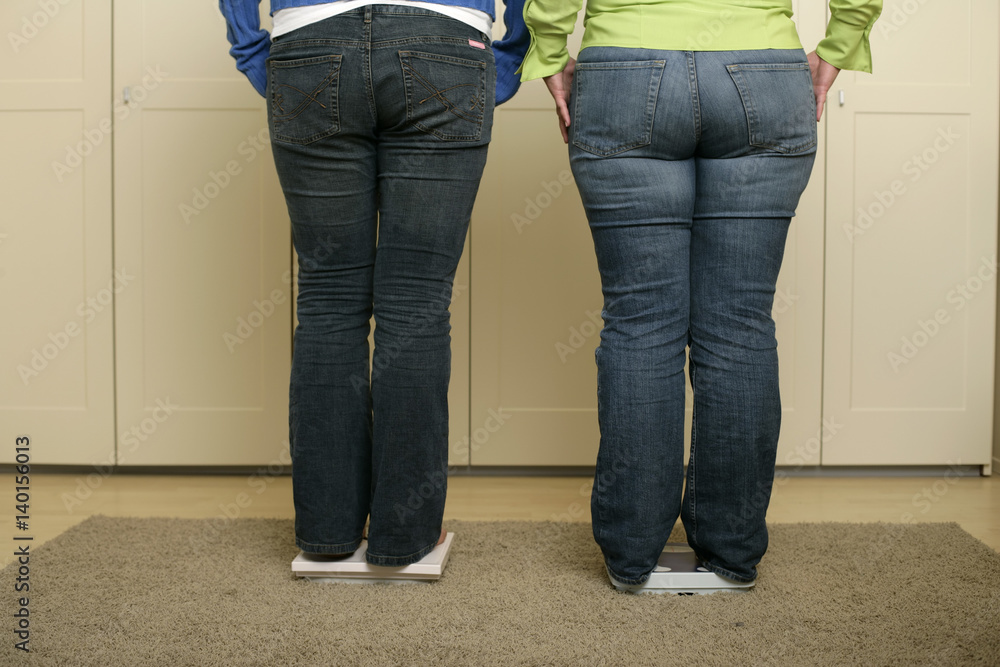 Two full figured women in blue jeans standing on scales (part of) Two full figured women in blue jeans standing on scales (part of)
