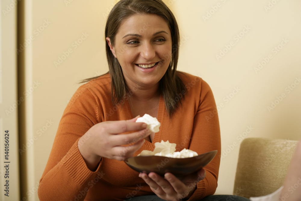 Overweight young woman with brown hair eating meringues Overweight young woman with brown hair eating meringues