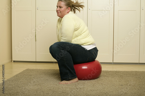 Overweight young woman with blond hair is sitting on a fitness ball photo