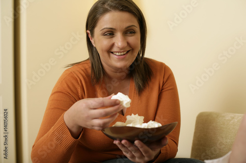 Overweight young woman with brown hair eating meringues