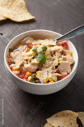 Chicken Tortilla Soup on wooden background with chips with spoon