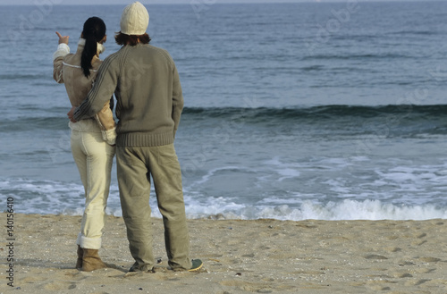 Young auburn-haired Man holding a brownhaired young Woman to his Arm - Love - Togetherness - Beach