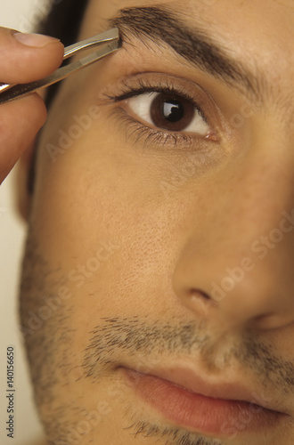 Man plugging his Eyebrow with Tweezers - Vanity - Beauty photo