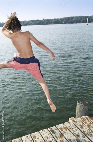 Boy jumping into Water from a wooden Footbridge - Saltation - Fun - Summer - Swimming photo