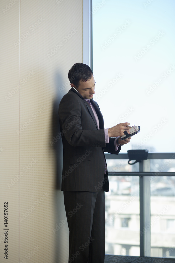 Businessman phoning with a mobile phone while reading diary Businessman phoning with a mobile phone while reading diary