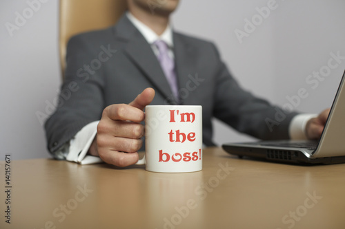 Businessman using laptop, I'm the boss! Coffee mug in foreground