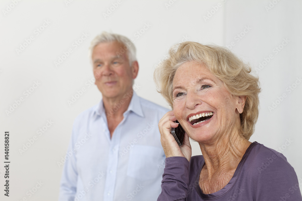 Senior woman on the phone with man in background Senior woman on the phone with man in background