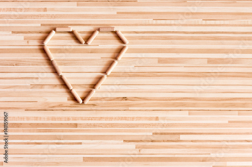 Heart composed of wooden dowels on wooden background