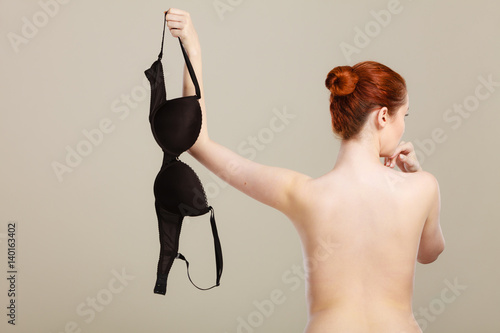 Naked woman holds black bra in hand
