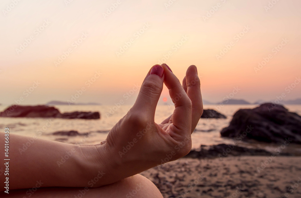 Woman hand exercising yoga in Sunrise at sea Woman hand exercising yoga in Sunrise at sea