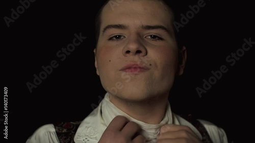 portrait of a gay man who looks in the camera over black background and begins to strangle himself. Close-up over black background