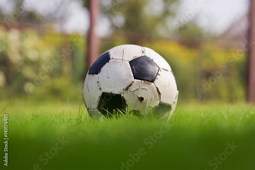 Old Soccer ball on a green grass. Football on a sports field. Sunny day. Summer time. Sporting goods. Closeup © KatiaMakarova