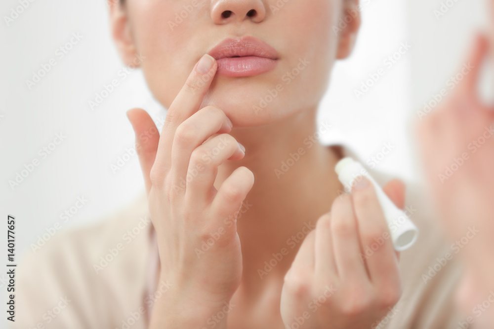 Woman applying hygienic lip balm near mirror - obrazy, fototapety, plakaty 