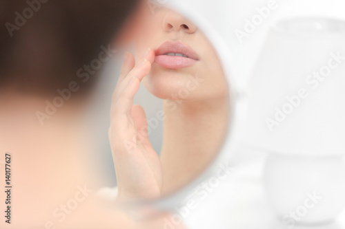 Young woman with cold sore looking in mirror at home