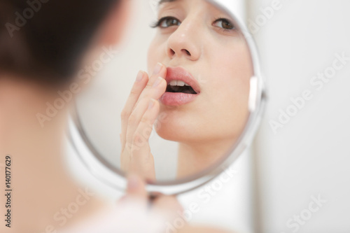 Young woman with cold sore looking in mirror at home photo