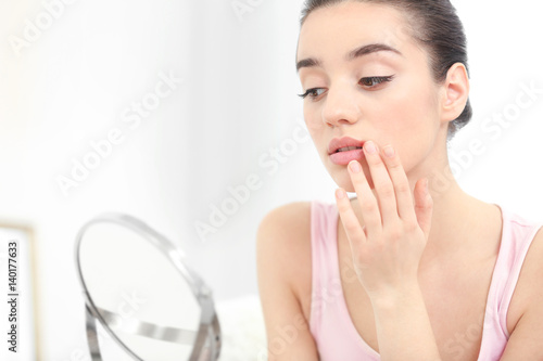 Young woman with cold sore looking in mirror at home photo