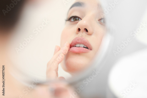 Young woman with cold sore looking in mirror at home photo