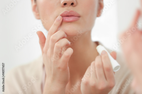 Murais de parede Woman applying hygienic lip balm near mirror