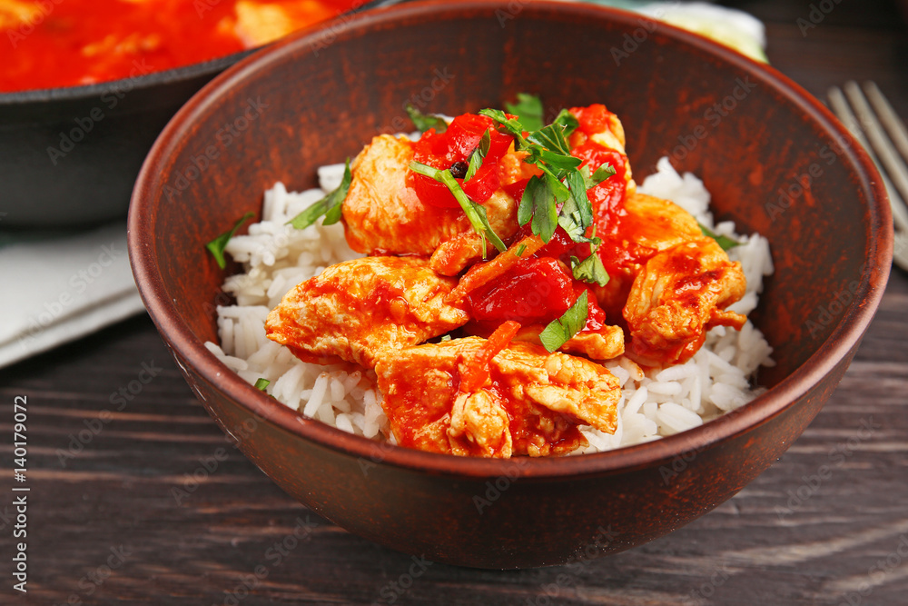 Portion of chicken tikka masala and rice in bowl on wooden table Portion of chicken tikka masala and rice in bowl on wooden table