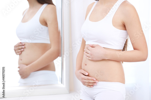 Beautiful pregnant woman standing near mirror in light room