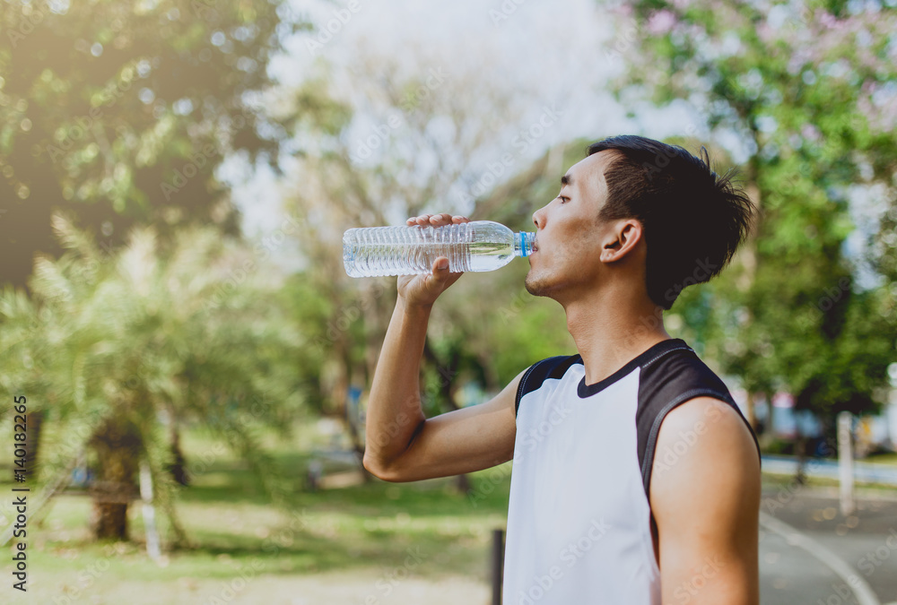 Sports man drinking water after exercising on background of green trees. Sports man drinking water after exercising on background of green trees.