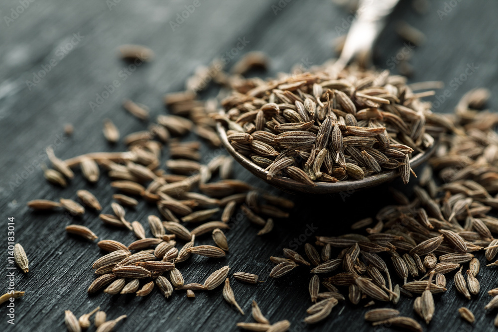 Cumin seeds in metal spoon on a wooden table, horizontal, selective focus