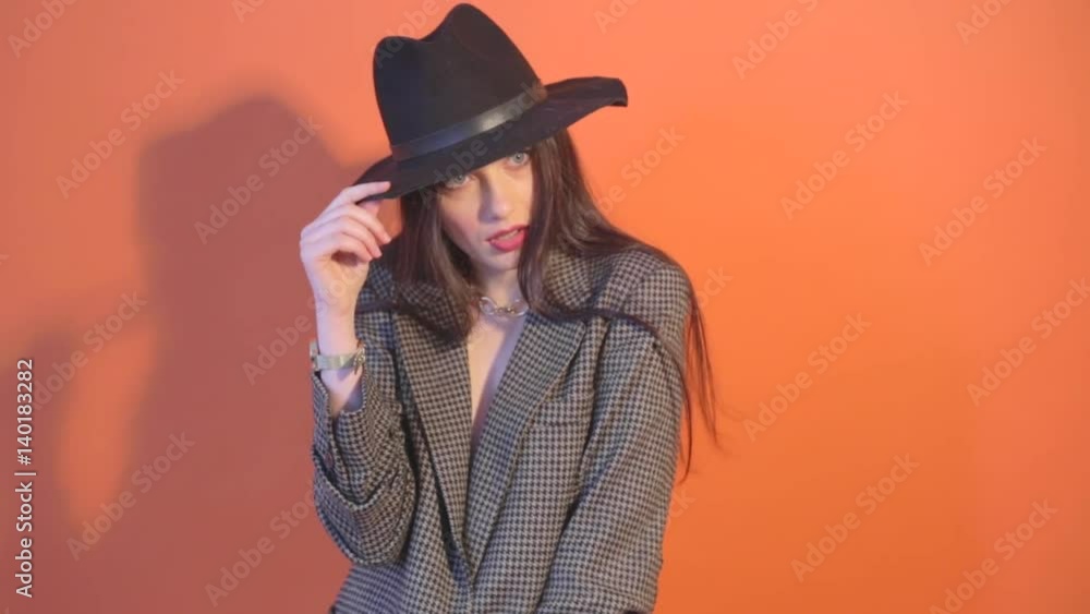 Woman in jacket touches the hat and posing during shooting time in studio Woman in jacket touches the hat and posing during shooting time in studio