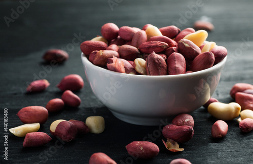Raw peanuts in bowl on a black wooden table