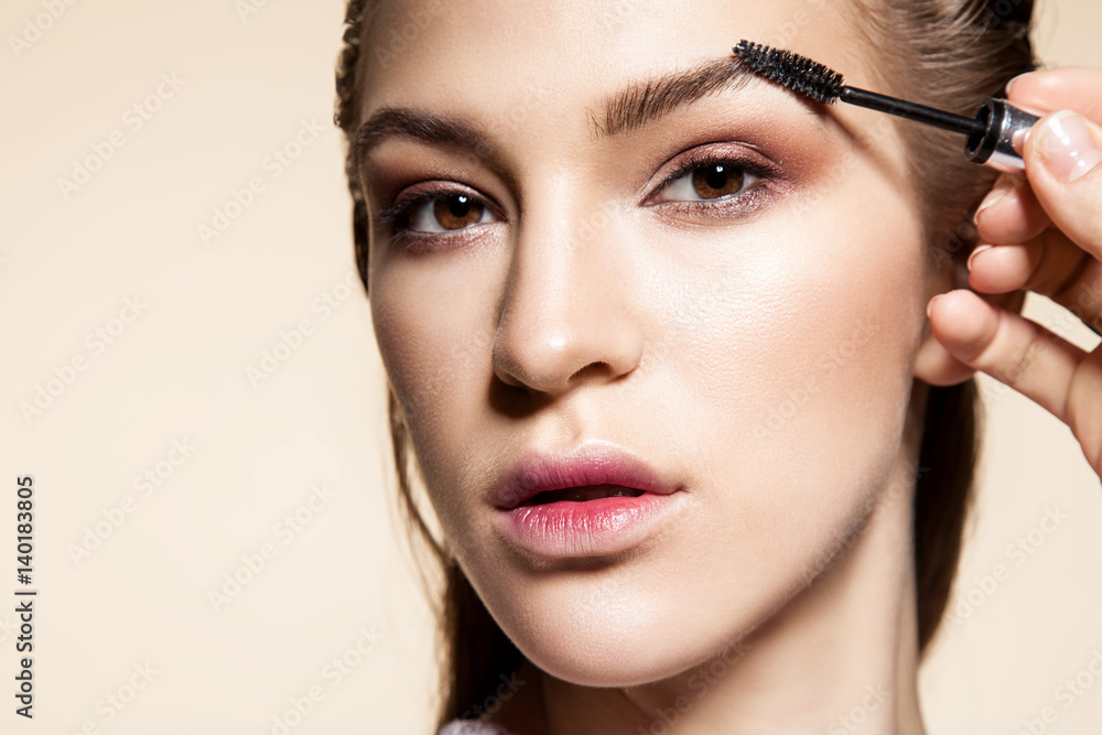 Close-up face of a girl making a brush shape eyebrows on a beige background
