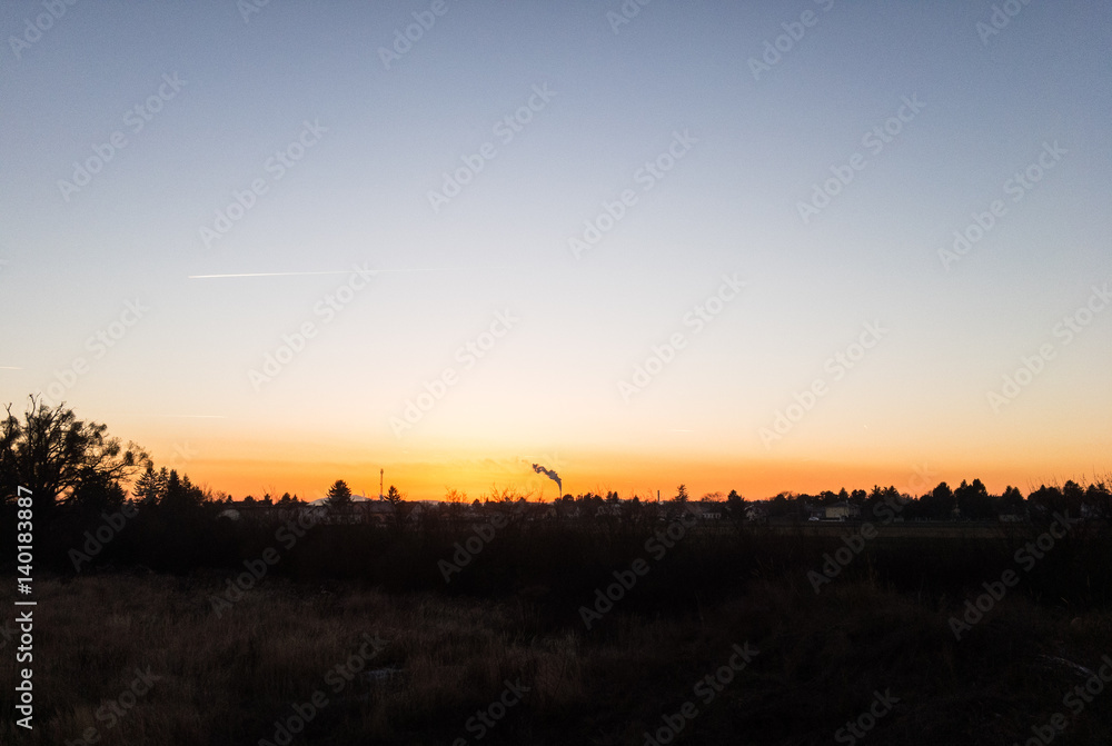 Sunset with a smoke rising from a smokestack in the distance