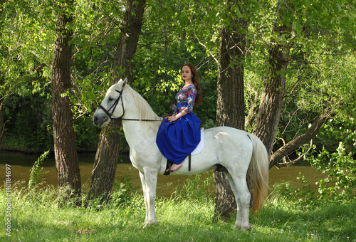 Young horsewoman in a blue dress on a white horse
