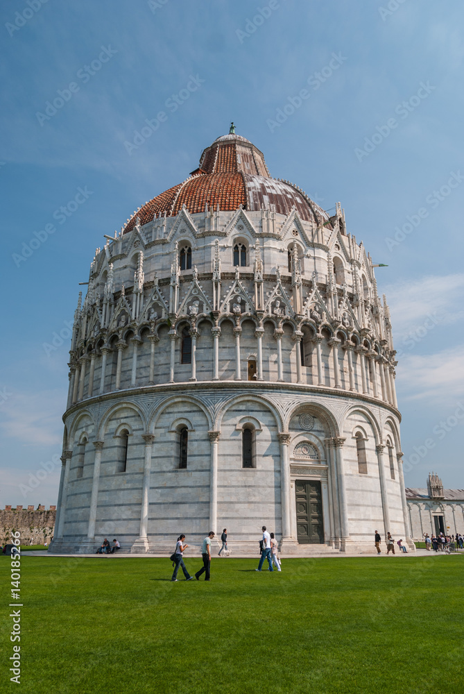 Baptistery of San Giovanni in Pisa, Italy on green field with tourist walking around it