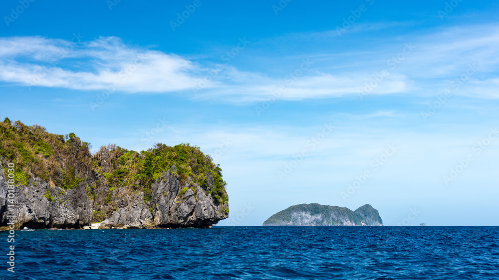 Distant view across a calm blue sea of some small rocky islands around El Nido, Philippines.