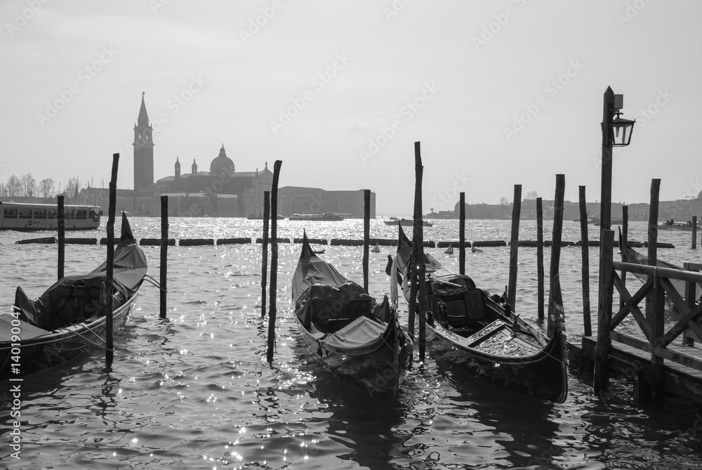 Gondolas in Venice, Italy tied to the pillars with San Giorgio church in the background, black and white