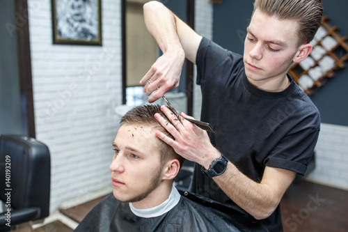 Great time at barbershop. Cheerful young bearded man getting haircut by hairdresser while sitting in chair at barbershop